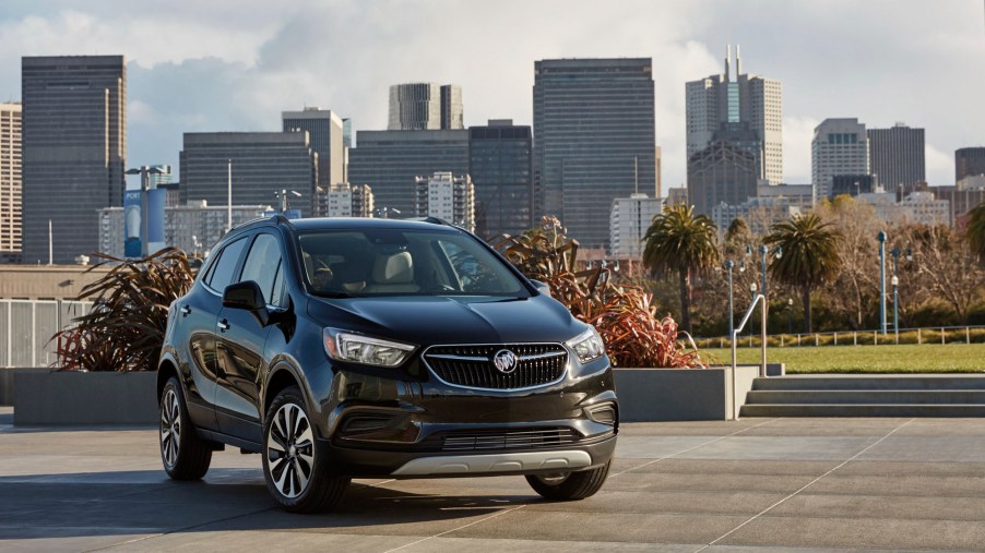 A dark-colored 2021 Buick Encore luxury subcompact SUV parked in front of a city skyline