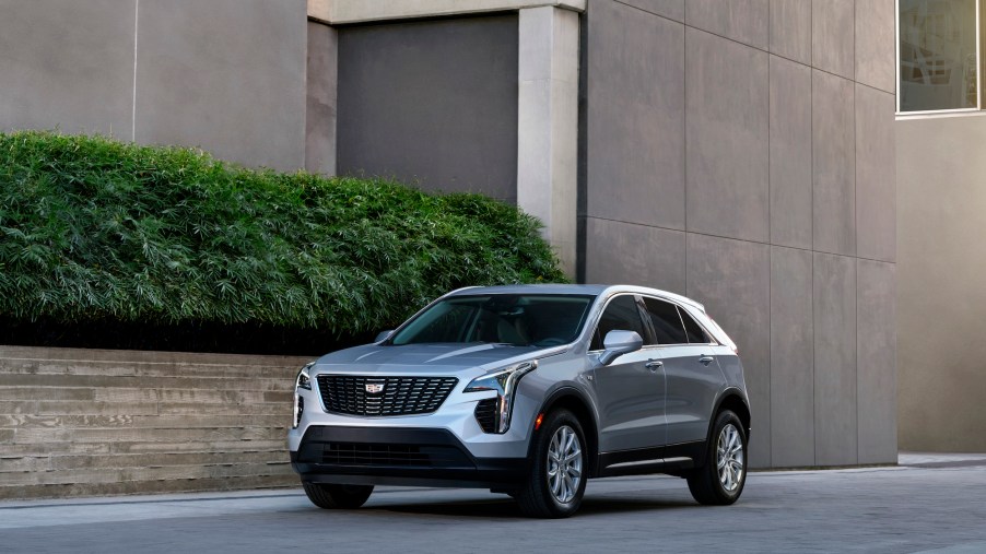 A silver 2021 Cadillac XT4 luxury compact crossover SUV parked next to a brownish-gray concrete modern building with a green hedge
