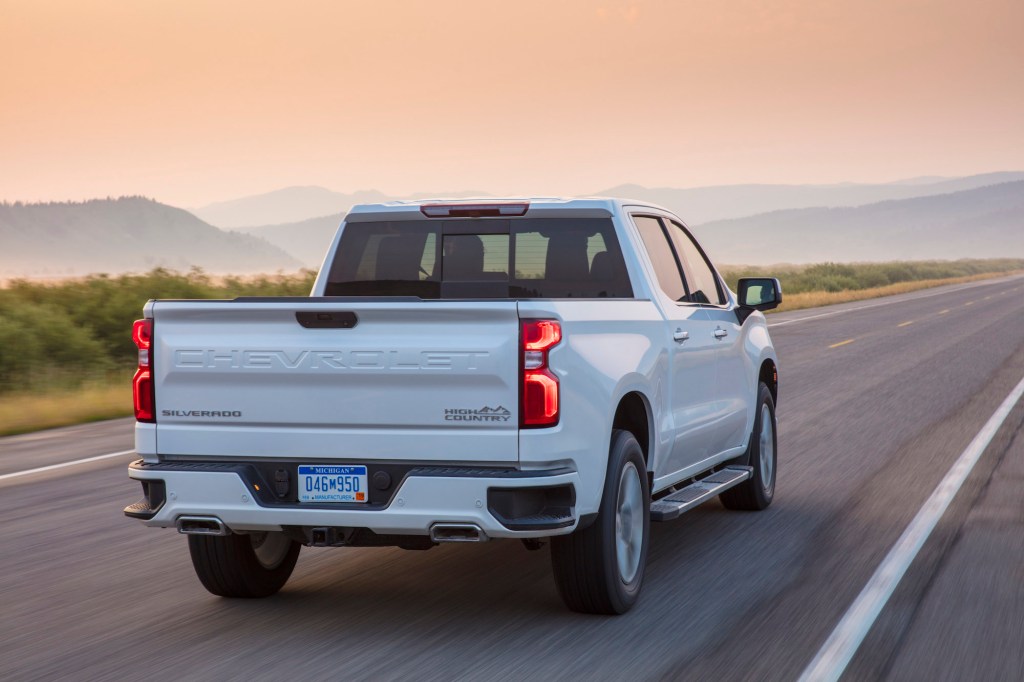 A white 2021 Chevy Silverado High Country four-door pickup truck traveling on a two-lane highway toward mountains on a foggy day