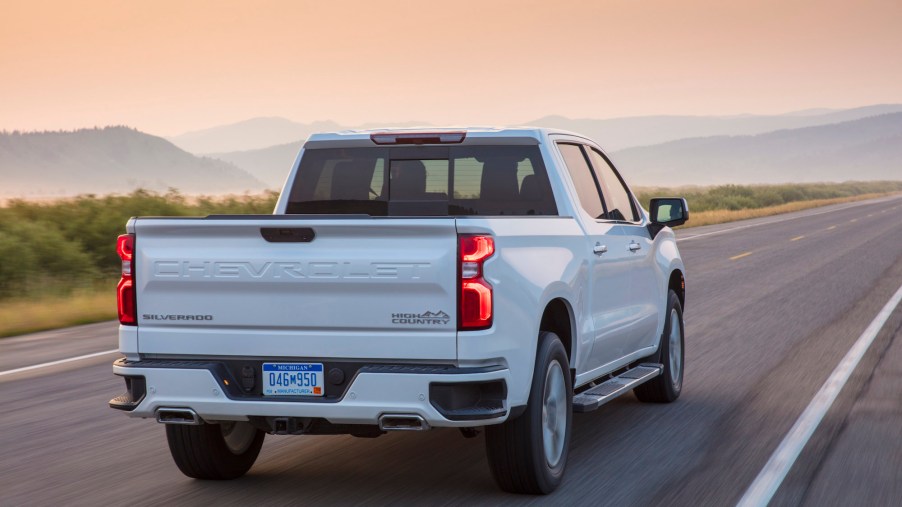 A white 2021 Chevy Silverado High Country four-door pickup truck traveling on a two-lane highway toward mountains on a foggy day