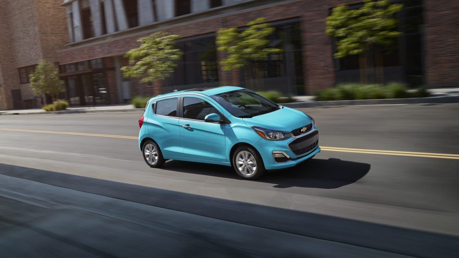 A blue Chevy Spark driving down a downtown street