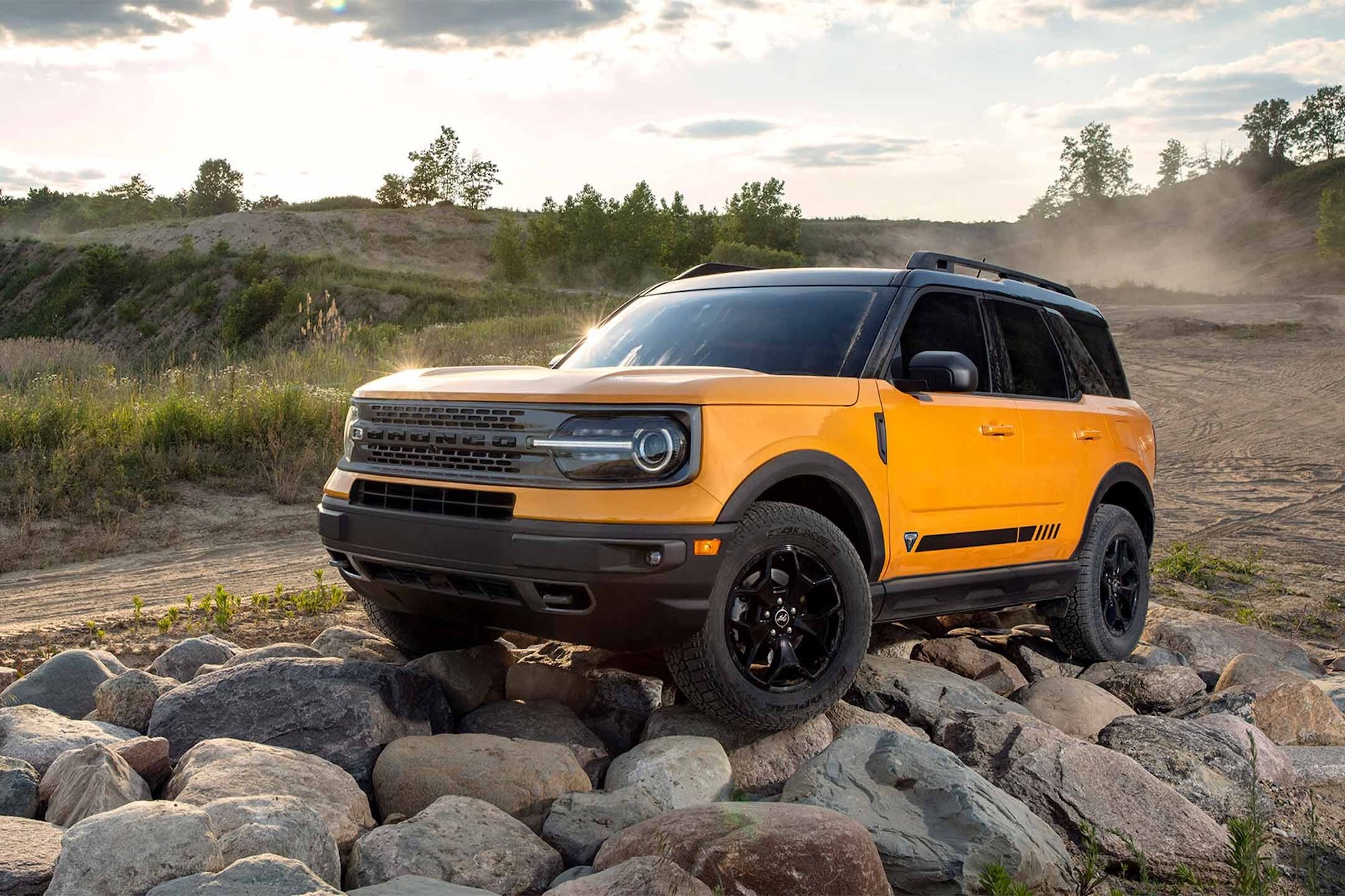An orange metallic 2021 Ford Bronco Sport compact crossover SUV parked on rocks beside a dirt road