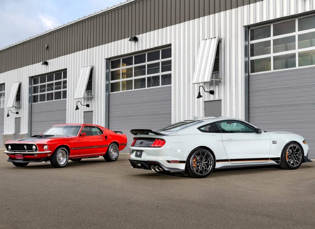 A gray 2021 Ford Mustang Mach 1 with the Handling Package parked with a red 1969 Ford Mustang Mach 1 next to a garage