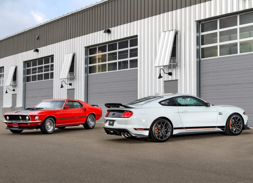 A gray 2021 Ford Mustang Mach 1 with the Handling Package parked with a red 1969 Ford Mustang Mach 1 next to a garage
