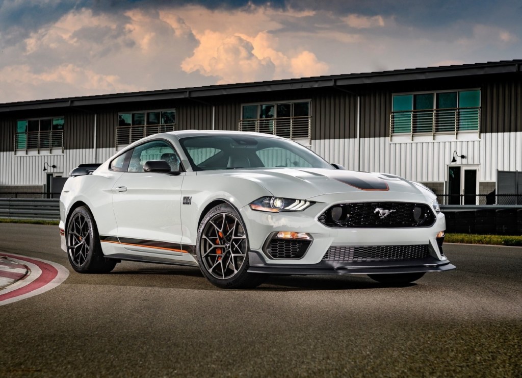 A gray-with-black-and-orange-stripes 2021 Ford Mustang Mach 1 on a track by a garage