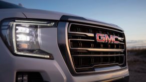 The right front headlight and grille of a pearl-white 2021 GMC Yukon AT4 full-size SUV