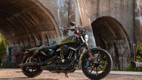 A dark-green 2021 Harley-Davidson Iron 883 by a river-bridge tunnel