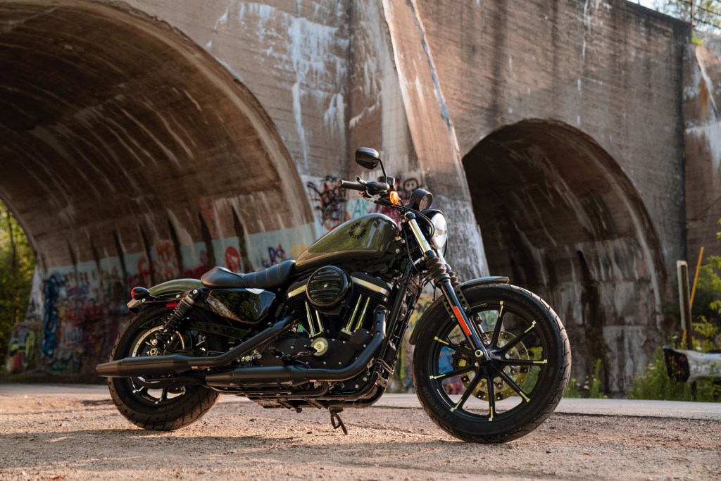 A dark-green 2021 Harley-Davidson Iron 883 by a river-bridge tunnel