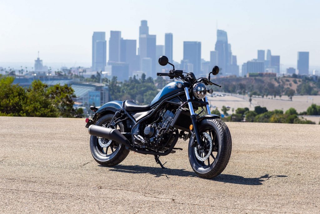 A dark-blue 2021 Honda Rebel 300 parked in a lot overlooking a city