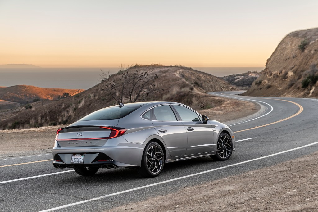 A silver 2021 Hyundai Sonata N Line midsize sedan out for a spin on a curvy two-lane mountain highway overlooking an ocean