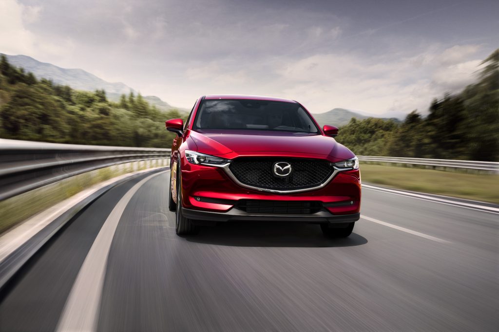 A front view of a red 2021 Mazda CX-5 compact crossover SUV traveling on a two-lane highway through the mountains