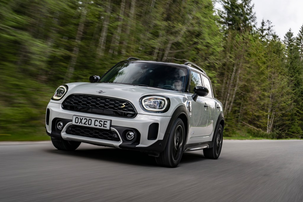 A white 2021 Mini Cooper Countryman compact crossover SUV traveling on a paved road along pinetrees