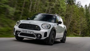 A white 2021 Mini Cooper Countryman compact crossover SUV traveling on a paved road along pinetrees