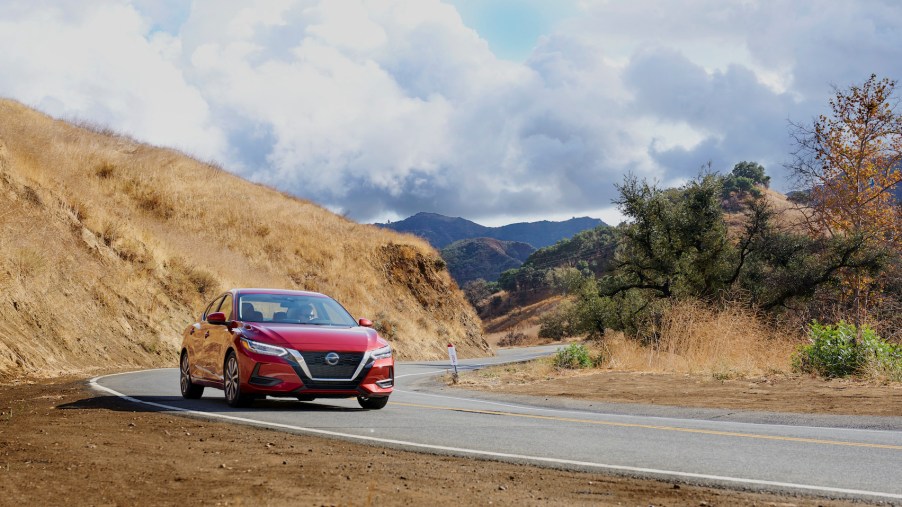 A red 2021 Nissan Sentra compact sedan travels on a winding two-lane mountain road