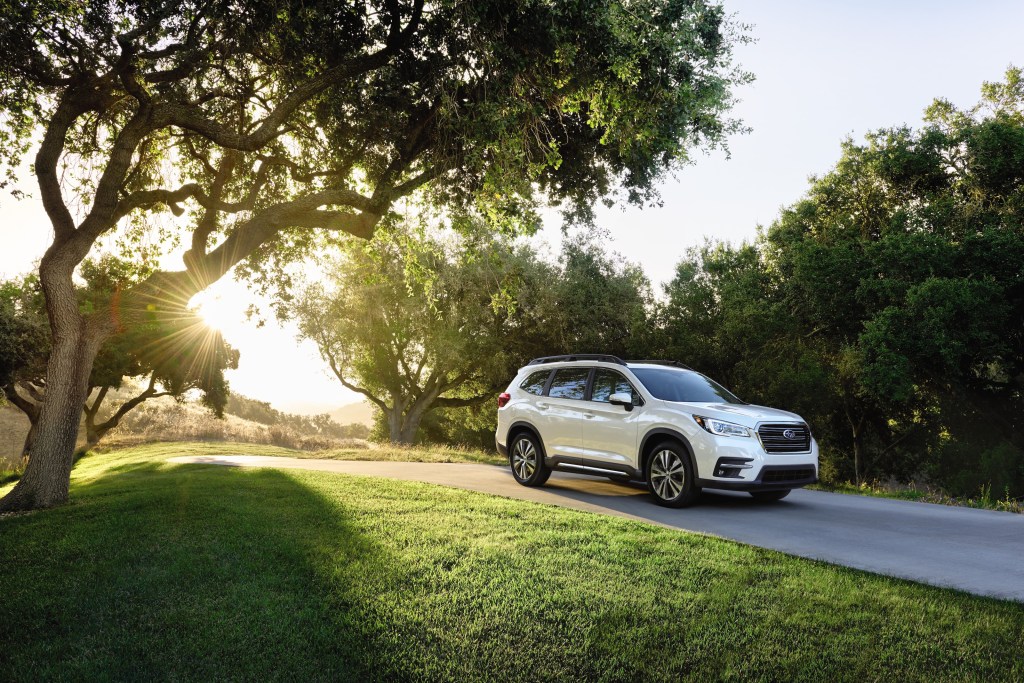 A white 2021 Subaru Ascent SUV driving down a tree-lined road