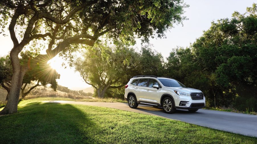 a white 2021 subaru ascent, trim level base, driving down a tree-lined road