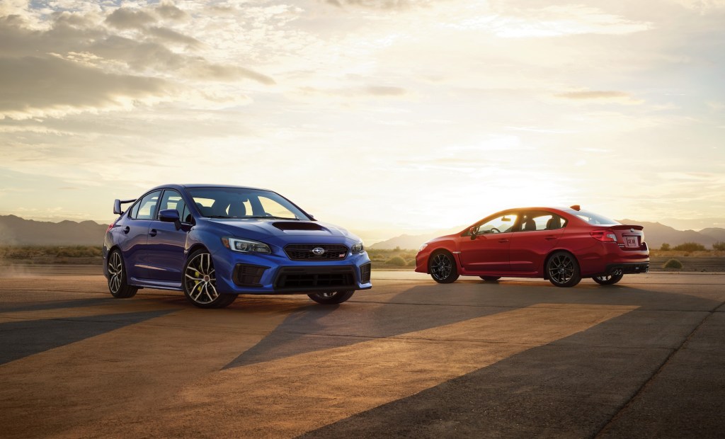 A blue 2021 Subaru WRX STI and a red WRX parked on asphalt in front of mountains