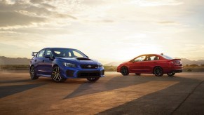 A blue 2021 Subaru WRX STI and a red WRX parked on asphalt in front of mountains
