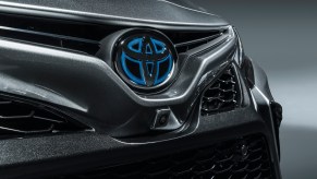 A dark-gray metallic 2021 Toyota Camry Hybrid sedan's honeycomb grille bears a silver and blue Toyota logo