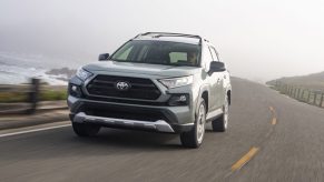 A gray and white 2021 Toyota RAV4 Adventure compact SUV traveling on a two-lane road overlooking a large body of water on a foggy day