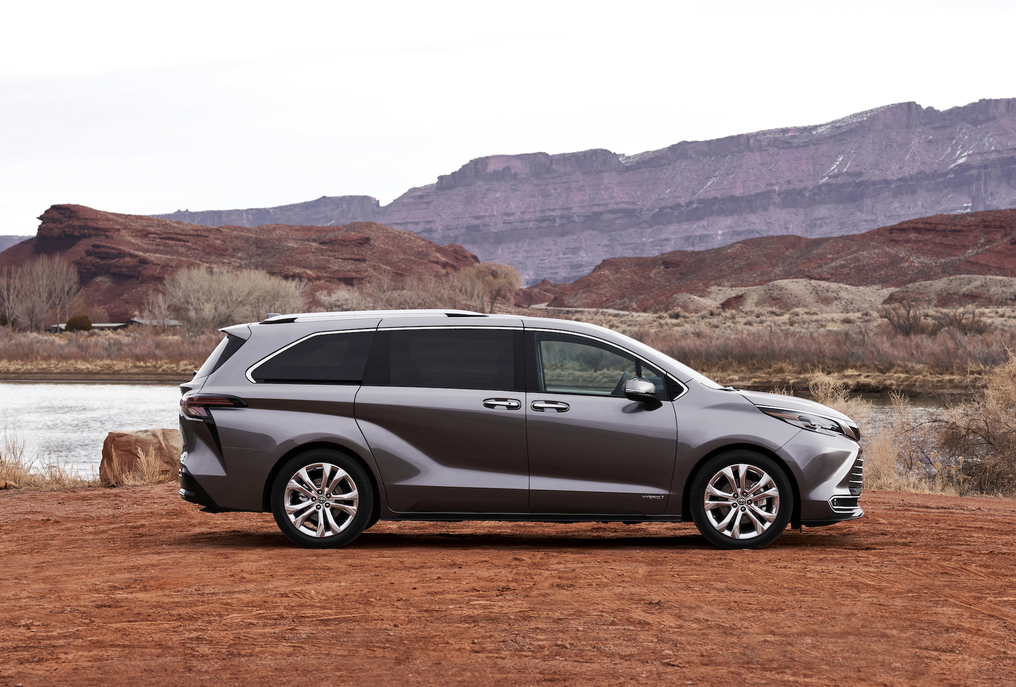 A pewter-colored 2021 Toyota Sienna Platinum hybrid minivan parked in red dirt and a small lake in front of mountains