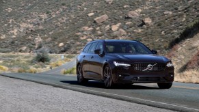 A black 2021 Volvo V90 station wagon on a two-lane mountain highway