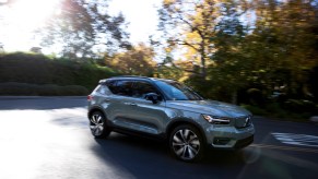 A gray 2021 XC40 Recharge electric compact crossover SUV turning a corner on a foliage-lined street