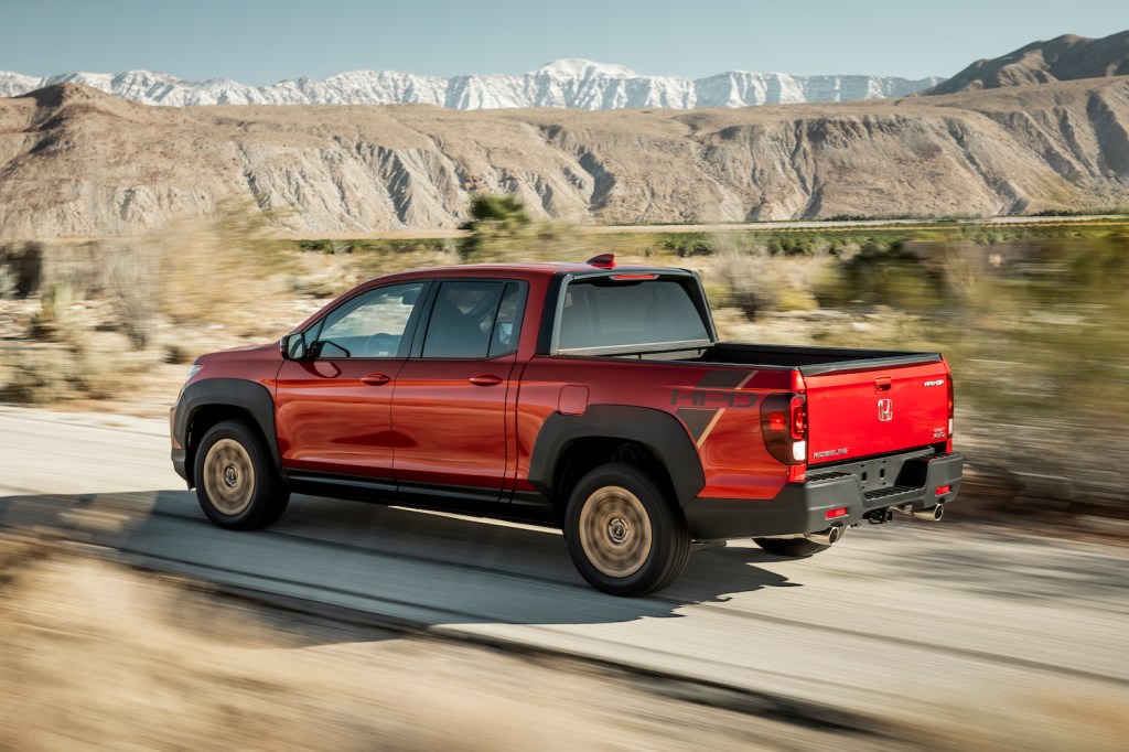 A red 2021 Ridgeline Sport with HPD Package driving on a dirt road makes it easier to see why Consumer Reports ranked this as the best pickup truck.