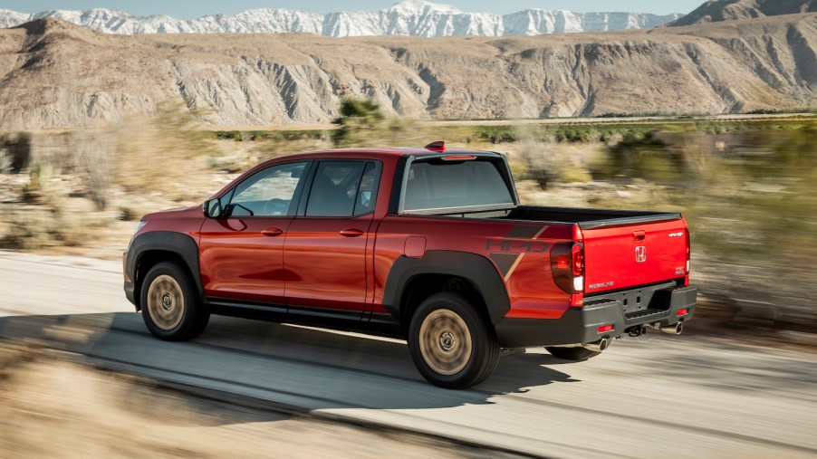 A red 2021 Ridgeline Sport with HPD Package driving on a dirt road