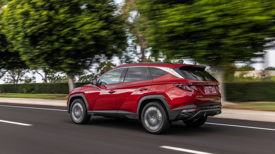 A red 2022 Hyundai Tucson travels on a highway lined with trees, grass, and a hedge