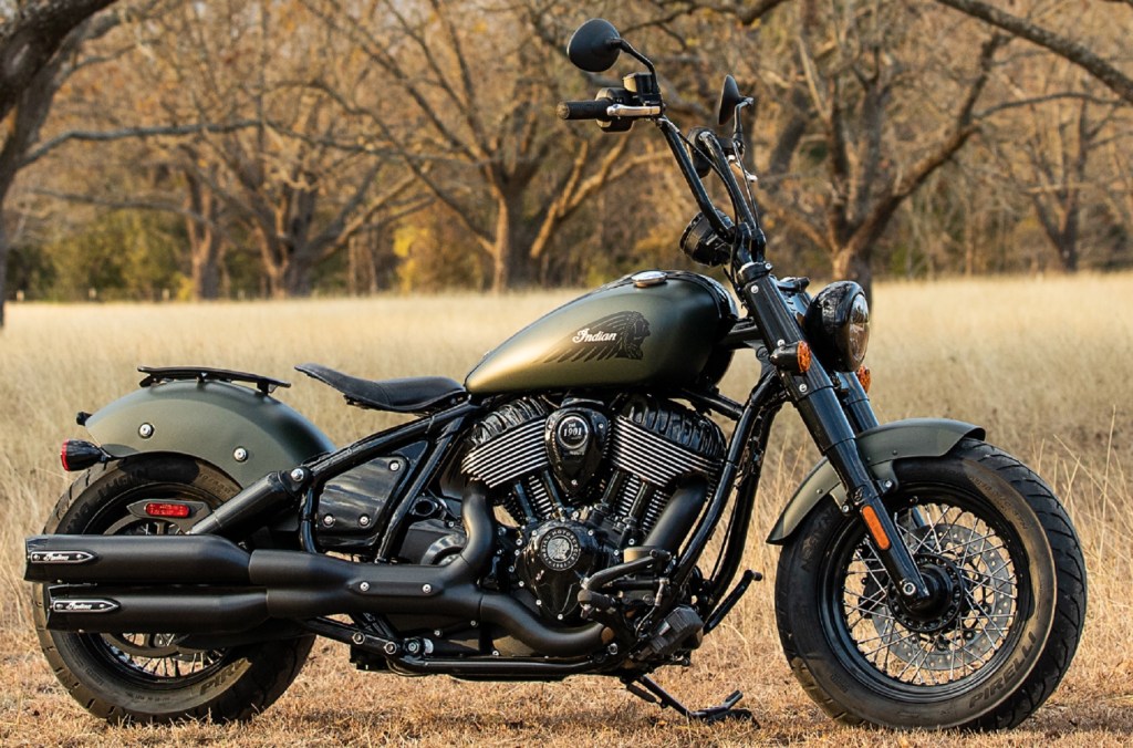 A matte-green 2022 Indian Chief Bobber Dark Horse with Authentic Collection accessories in a forested field