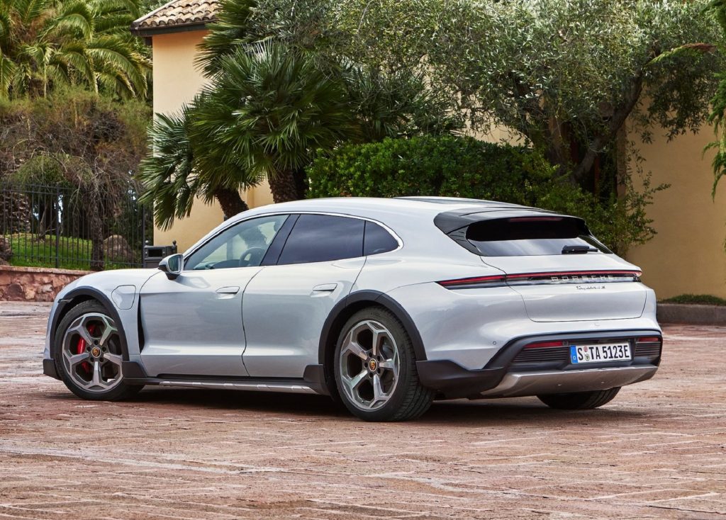 The rear 3/4 view of a silver 2022 Porsche Taycan 4S Cross Turismo parked by a palm-tree-lined villa
