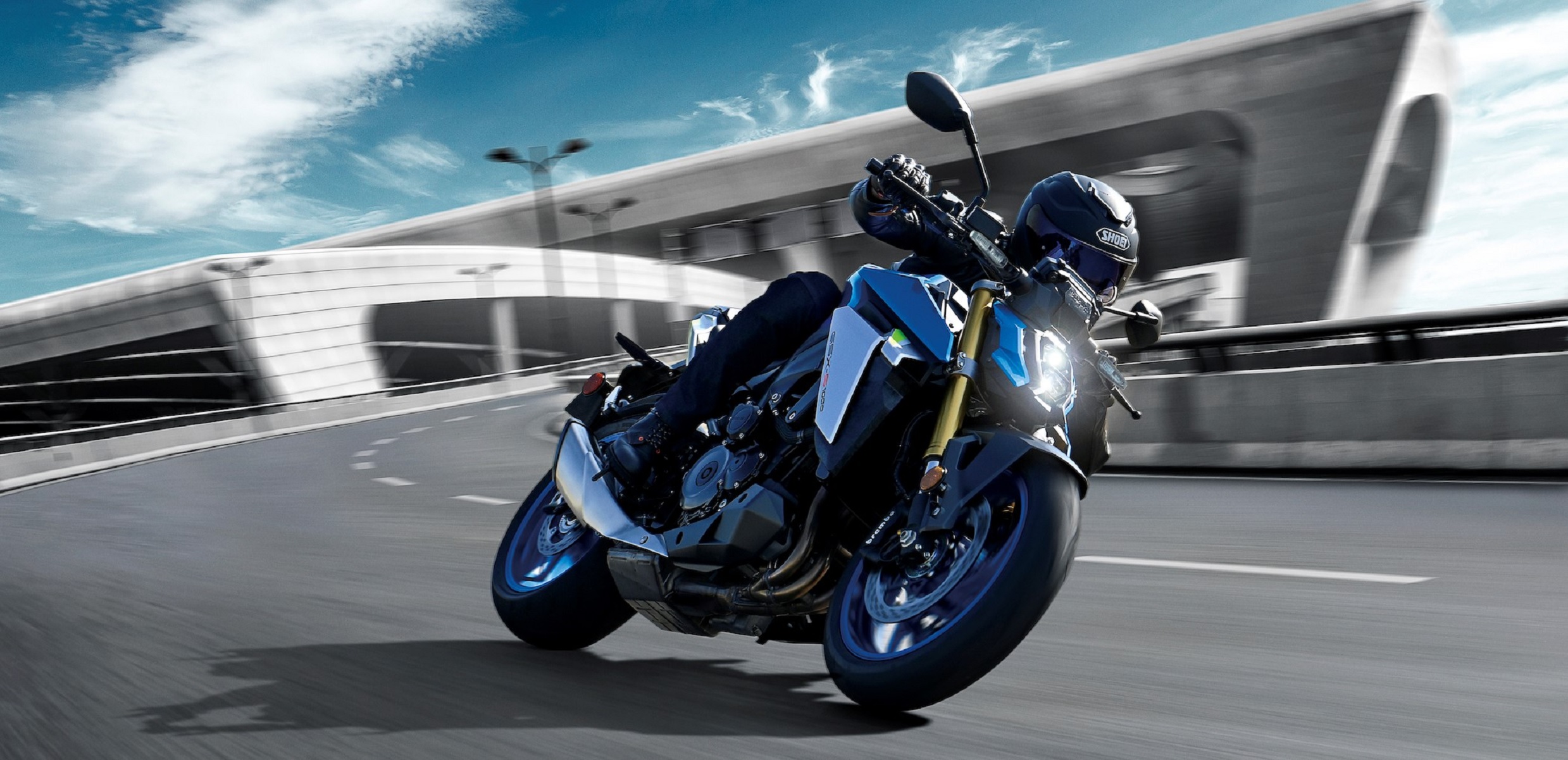 A black-clad rider taking a blue-and-silver 2022 Suzuki GSX-S1000 around a highway corner