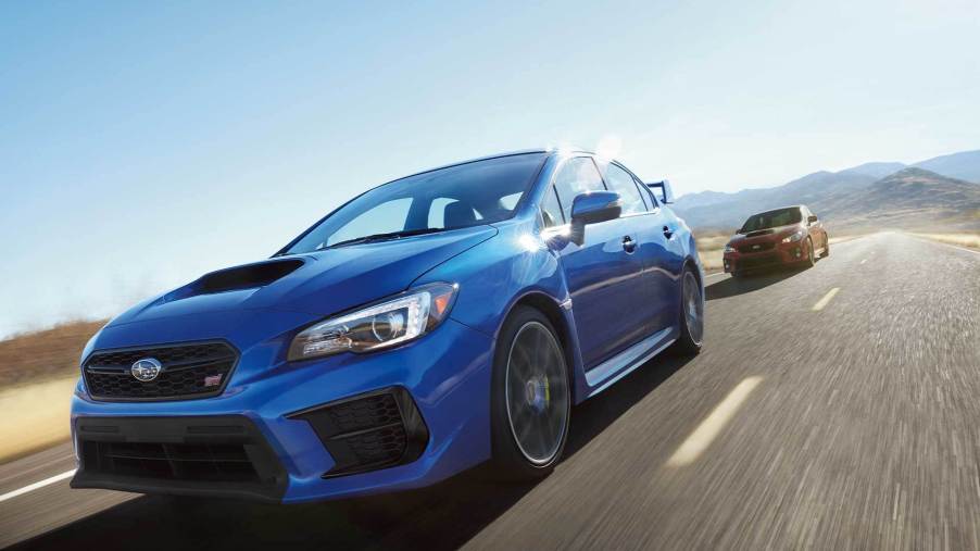 a classic blue 2021 Subaru WRX driving fast on a road with a red model close behind