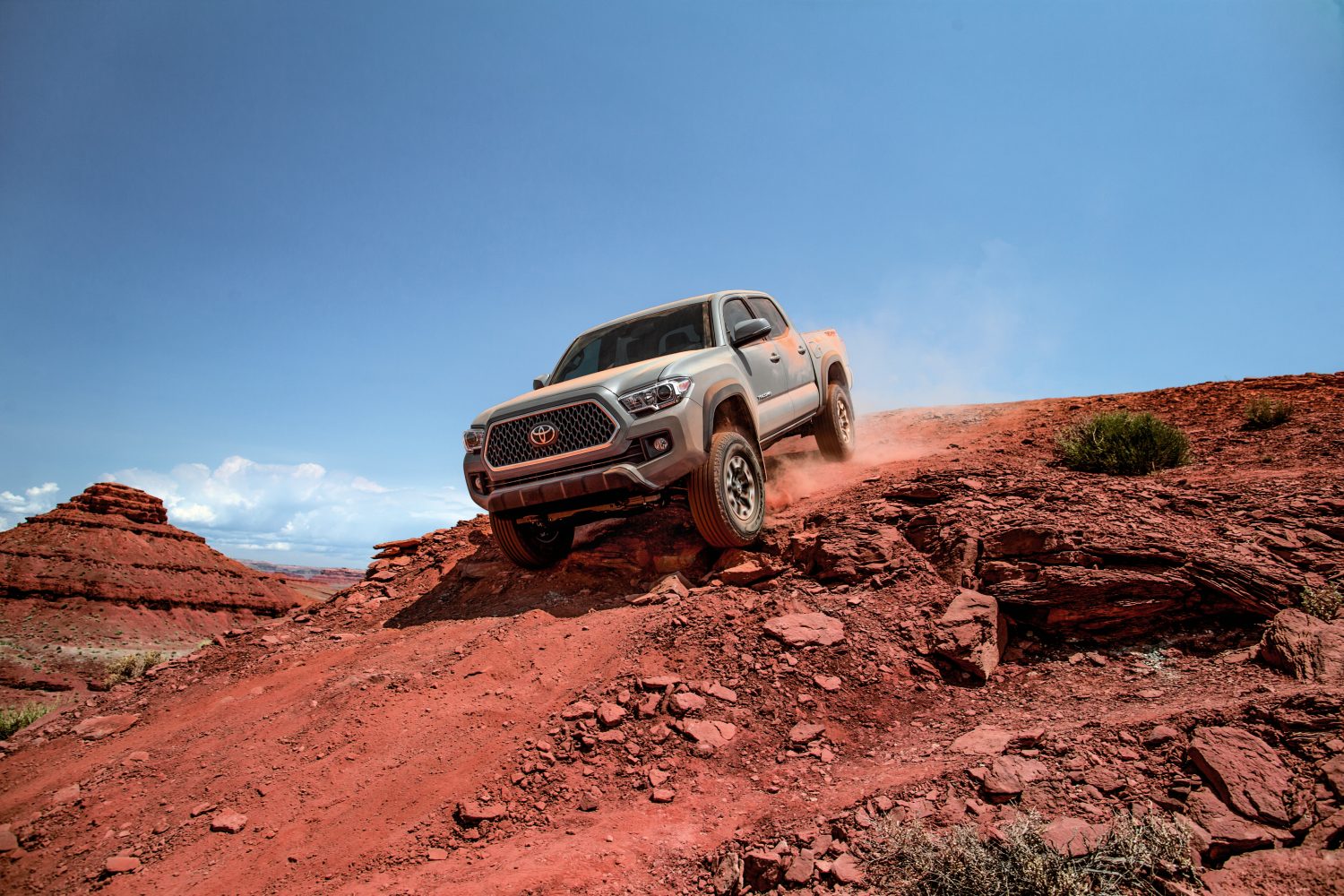 a gray 2018 model year Toyota Tacoma climbing down a sandy red incline on an off-road trail in the desert. 