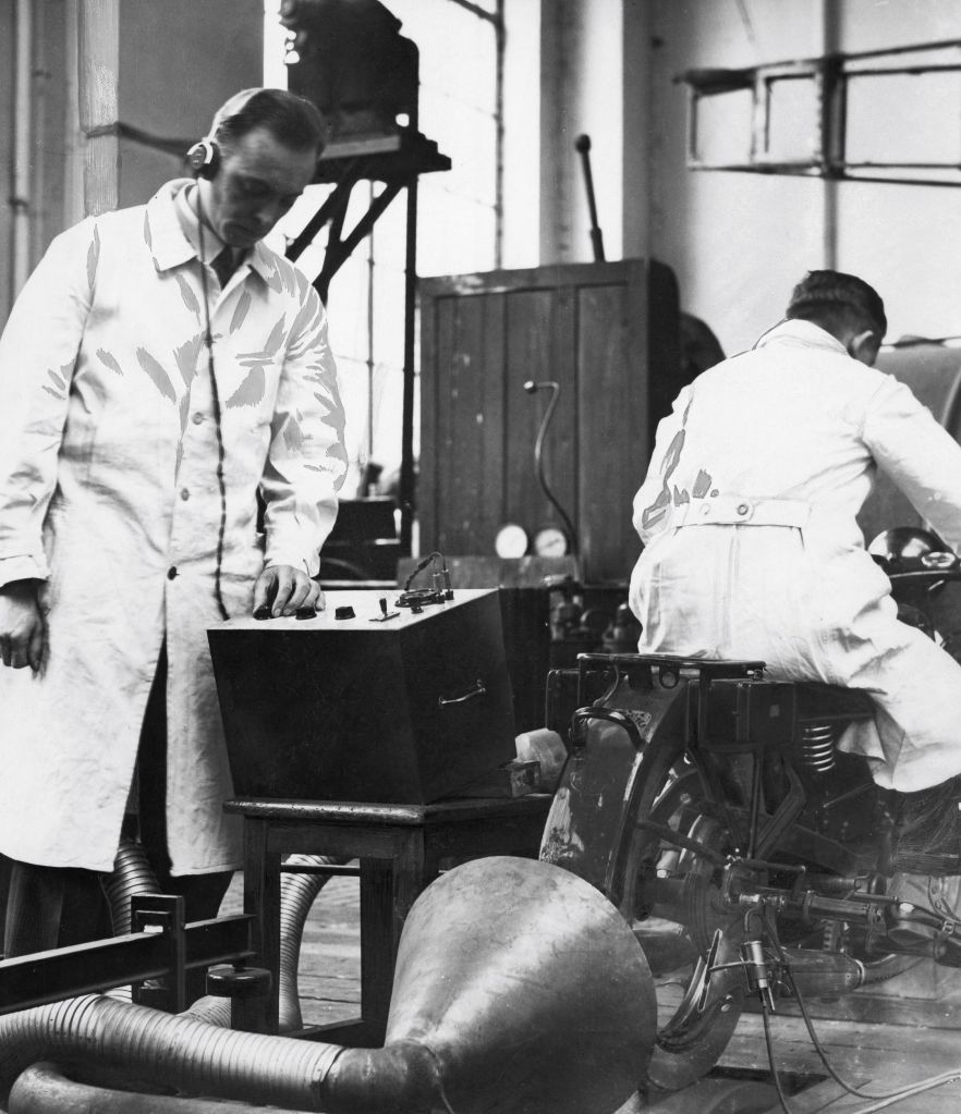 Two laboratory workers measure a 1933 motorcycle's emissions