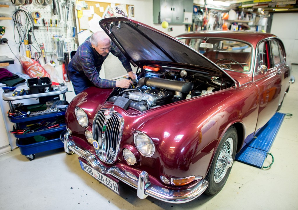 Vintage car collector Horst F. Beilharz examines the inline-six engine of his red Jaguar S-Type in his garage