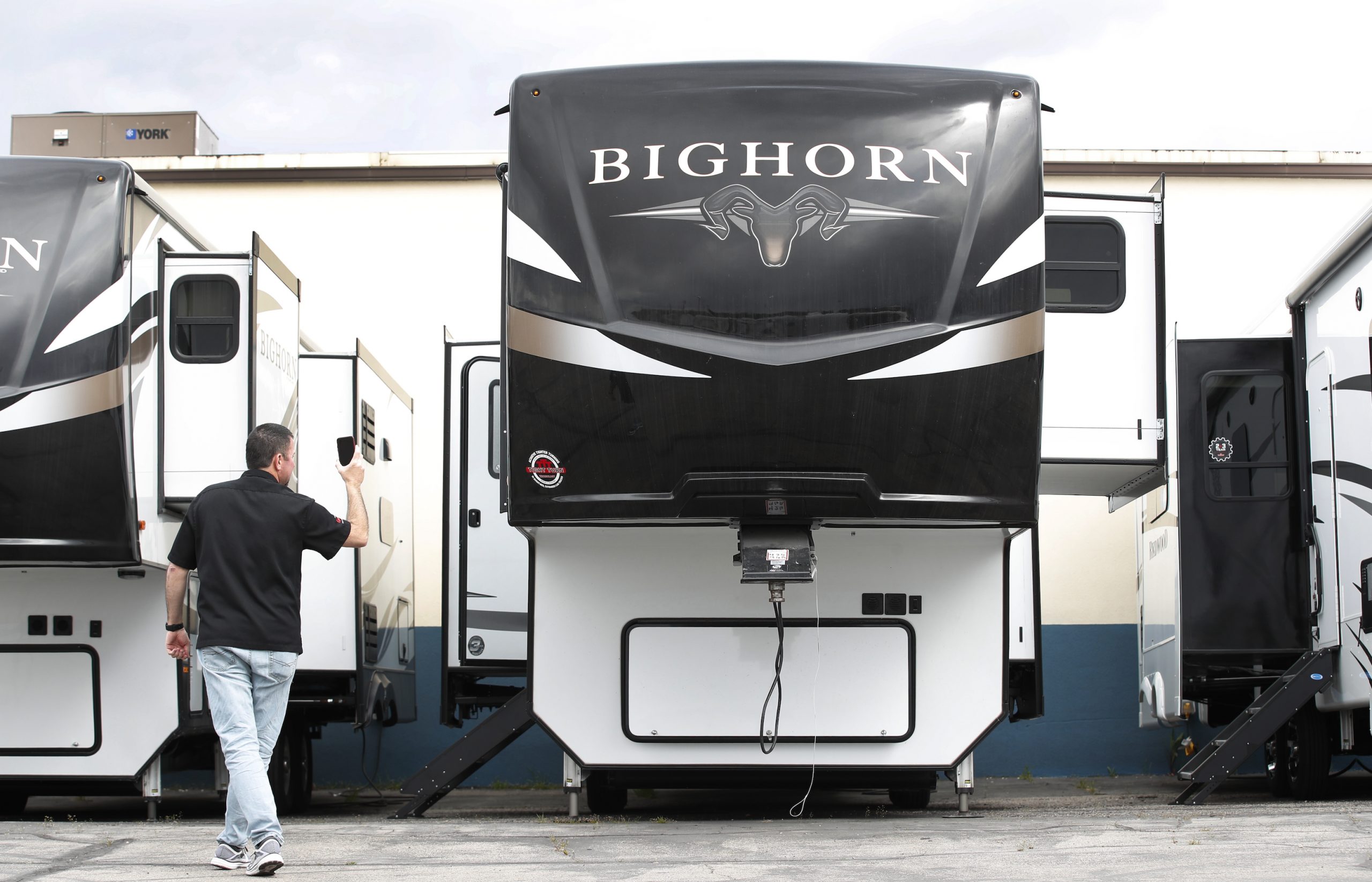 A salesperson holds a mobile device while using video chat to show a potential customer a Heartland Recreational Vehicles LLC Big Horn travel trailer at Motor Sportsland RV dealership