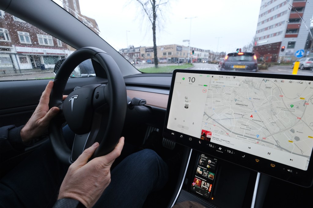 An image of a person steering a Tesla through a city.