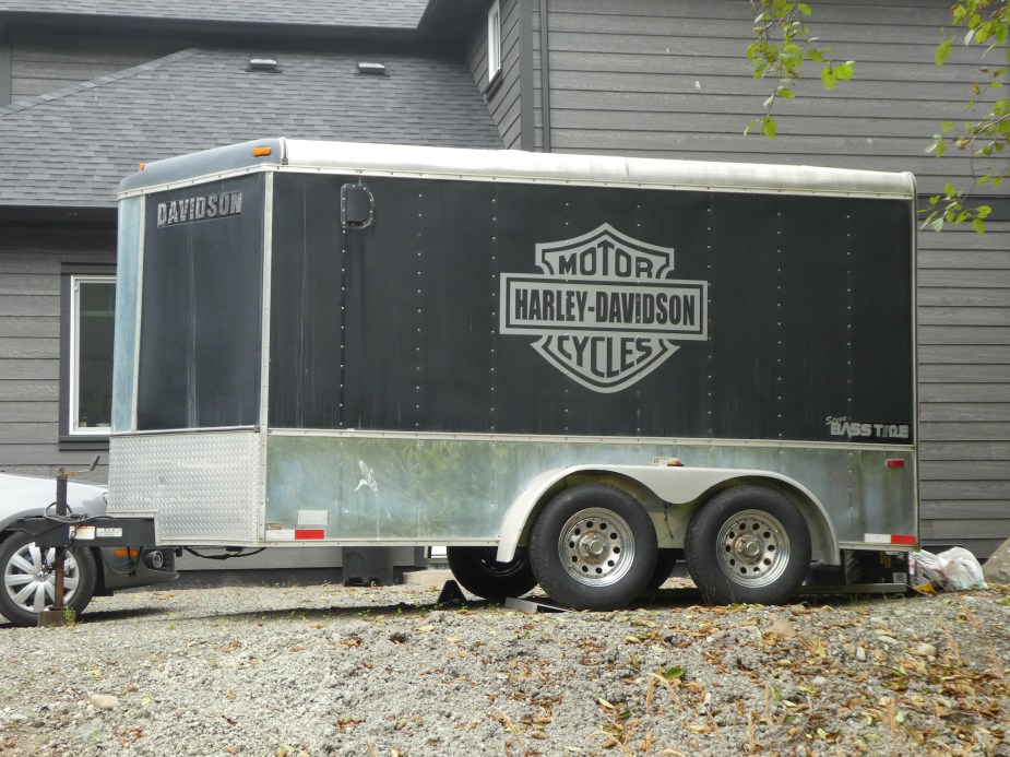 A silver and black Harley-Davidson toy hauler travel trailer parked outside a home