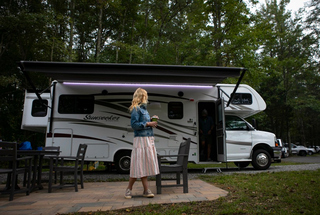 A woman in a pink dress stands in front of an RV at an RV campground.