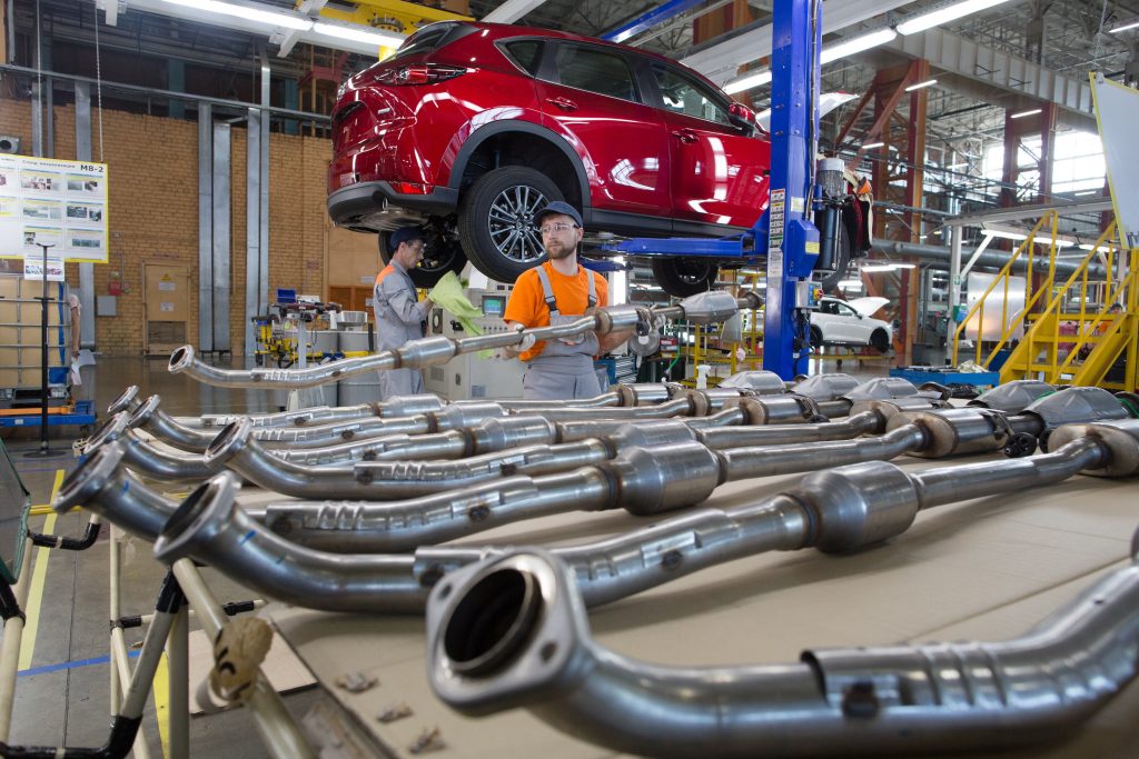 A worker handles an exhaust piping unit ready for installation into a red Mazda Motor Corp. CX-5 sports utility vehicle (SUV) on the assembly line at the Mazda Sollers Manufacturing Rus LLC plant