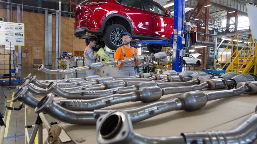 A worker handles an exhaust piping unit ready for installation into a red Mazda Motor Corp. CX-5 sports utility vehicle (SUV) on the assembly line at the Mazda Sollers Manufacturing Rus LLC plant