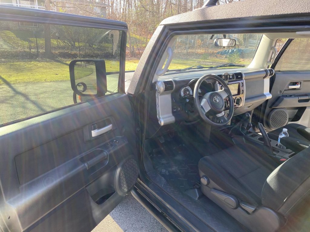 The front seats and dashboard of a modified 2007 Toyota FJ Cruiser parked by a backyard