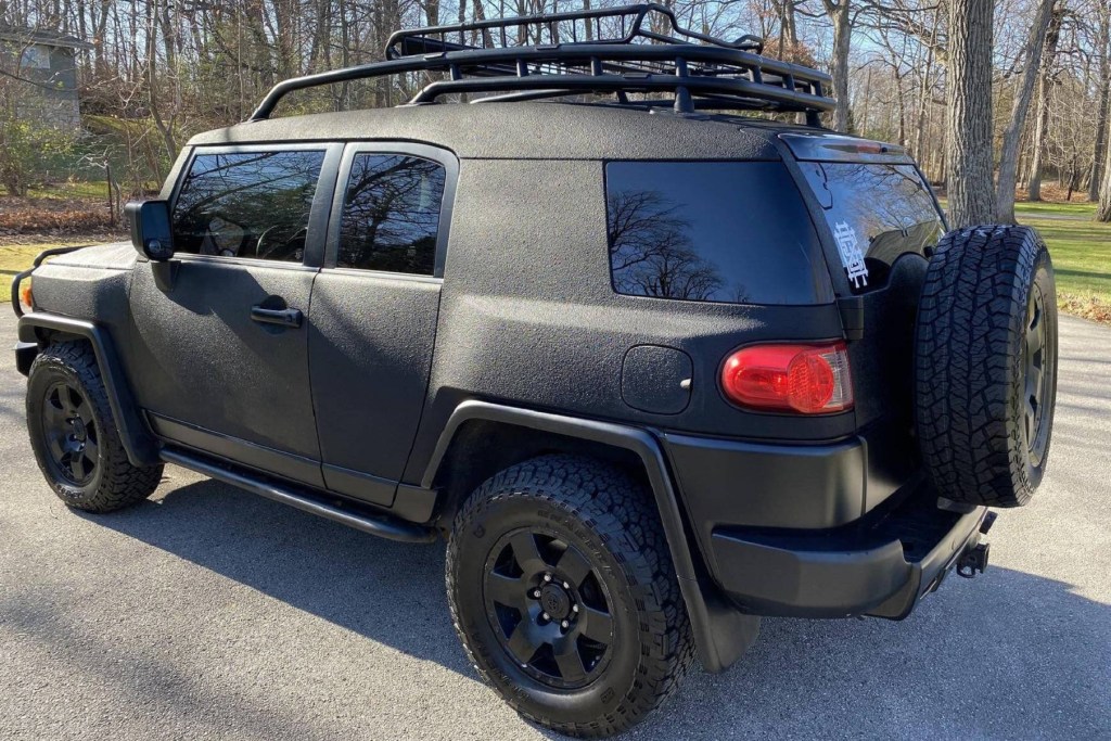 The rear 3/4 view of a black-Raptor-bedliner-sprayed modified 2007 Toyota FJ Cruiser parked in a driveway