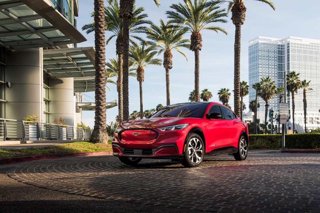 An image of a red 2021 Ford Mustang Mach-E outdoors near palm trees.