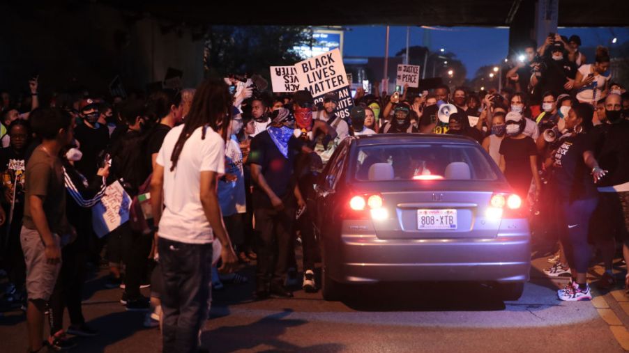 A car tries to drive through the crowd as demonstrators protest in the streets