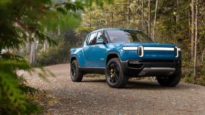 A blue Rivian R1T parked on a gravel road in a forest