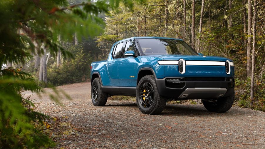 A blue Rivian R1T parked on a gravel road in a forest