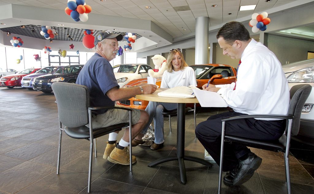 A couple sitting across from a car salesman while shopping for a car.